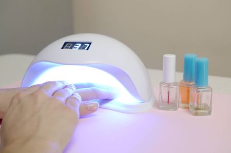 Hands of young woman at manicure procedure close up on pastel pink background. Woman Nail Polish process. Female using shellac uv led lamp for quick dryingの写真素材