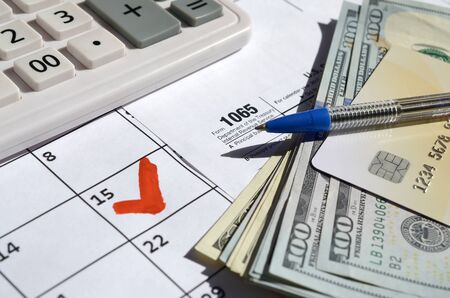 1065 Return of partnership income blank with dollar bills, calculator and pen on calendar page with...