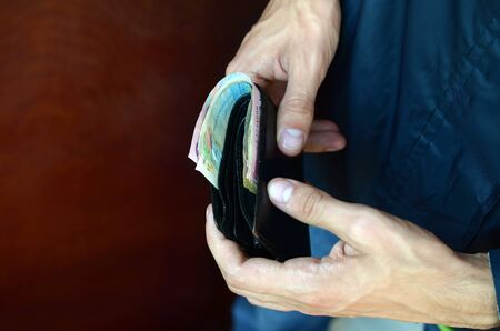 Man holds in hands black leather wallet with ukrainian money or thief who stole wallet full of...