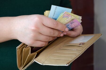 Female hands holding ukrainian hryvnia bills in small money pouch or wallet. Small salary in...