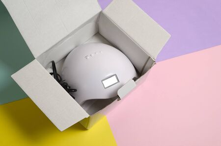 Unboxing of new UV LED nail lamp for curing process by gel method. Cardboard box on pastel multi...