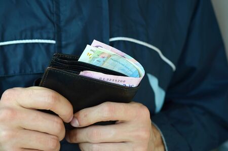 Man holds in hands black leather wallet with ukrainian money or thief who stole wallet full of...