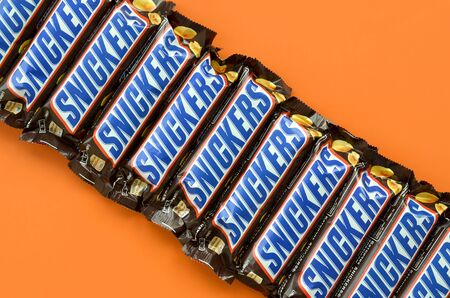 KHARKOV, UKRAINE - OCTOBER 2, 2019: Many Snickers chocolate bars lies on pastel orange paper....