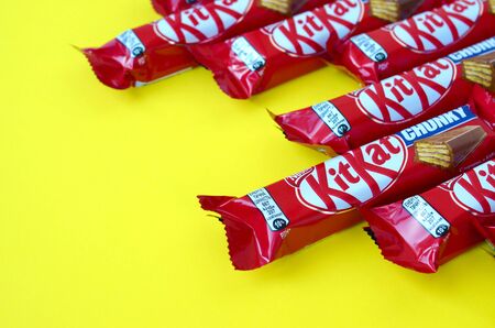 KHARKOV, UKRAINE - OCTOBER 17, 2019: Kit Kat chocolate bars in red wrapping lies on yellow background. Kit kat created by Rowntree's of York in United Kingdom and is now produced globally by Nestleのeditorial素材