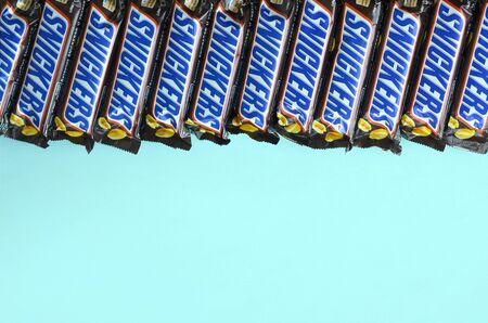KHARKOV, UKRAINE - OCTOBER 2, 2019: Many Snickers chocolate bars lies on pastel blue paper. Snickers bars are produced by Mars Incorporated. Snickers was created by Franklin Clarence Mars in 1930のeditorial素材