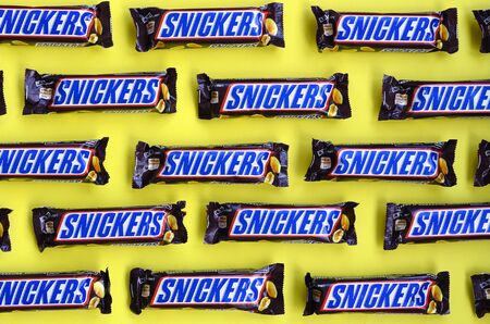 KHARKOV, UKRAINE - OCTOBER 2, 2019: Many Snickers chocolate bars lies on pastel yellow paper. Snickers bars are produced by Mars Incorporated. Snickers was created by Franklin Clarence Mars in 1930のeditorial素材