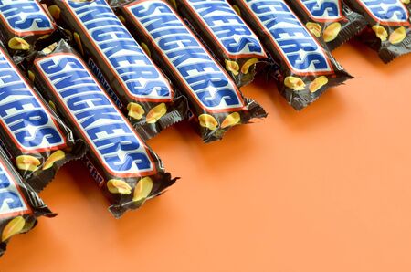 KHARKOV, UKRAINE - OCTOBER 2, 2019: Many Snickers chocolate bars lies on pastel orange paper. Snickers bars are produced by Mars Incorporated. Snickers was created by Franklin Clarence Mars in 1930のeditorial素材