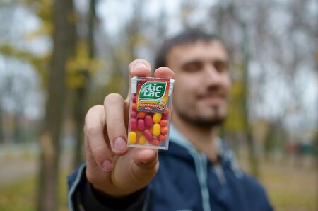KHARKOV, UKRAINE - OCTOBER 26, 2019: Young man shows new Tic tac hard mints package in autumn park. Tic tac is popular due its minty fresh taste by Ferrero since 1968のeditorial素材