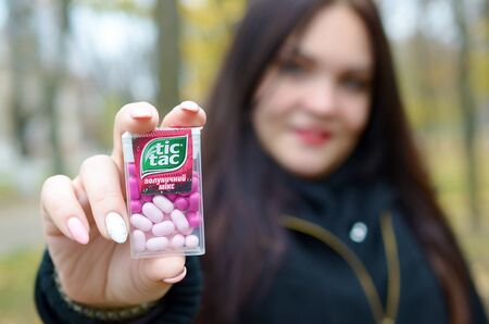 KHARKOV, UKRAINE - OCTOBER 26, 2019: Young woman shows new Tic tac hard mints package in autumn park. Tic tac is popular due its minty fresh taste by Ferrero since 1968のeditorial素材