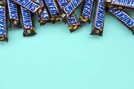 KHARKOV, UKRAINE - OCTOBER 2, 2019: Many Snickers chocolate bars lies on pastel blue paper. Snickers bars are produced by Mars Incorporated. Snickers was created by Franklin Clarence Mars in 1930のeditorial素材