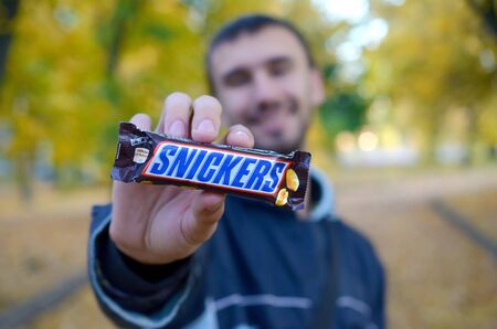 KHARKOV, UKRAINE - OCTOBER 8, 2019: A young caucasian bearded man shows Snickers chocolate bar in...