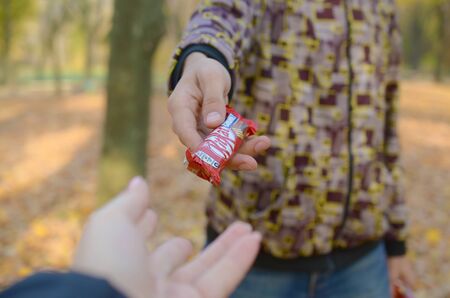 KHARKOV, UKRAINE - OCTOBER 21, 2019: A male hand passes the girl a Kit kat chocolate bar in an autumn park. The manifestation of kindness, treating with sweetsのeditorial素材