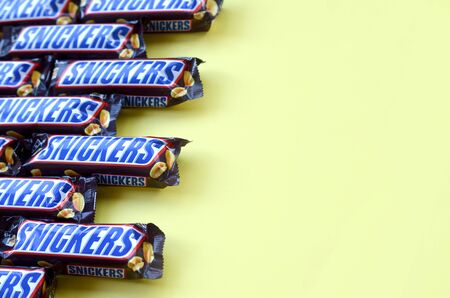 KHARKOV, UKRAINE - OCTOBER 2, 2019: Many Snickers chocolate bars lies on pastel yellow paper....