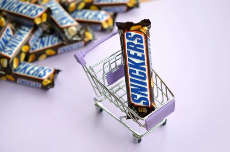 KHARKOV, UKRAINE - OCTOBER 2, 2019: Many Snickers chocolate bars stacked close up with shopping cart...