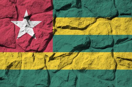 Togo flag depicted in paint colors on old stone wall close up. Textured banner on rock wall backgroundの写真素材