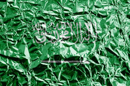 Saudi Arabia flag depicted in paint colors on shiny crumpled aluminium foil close up. Textured banner on rough backgroundの写真素材