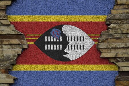 Swaziland flag depicted in paint colors on old stone wall close up. Textured banner on rock wall backgroundの写真素材