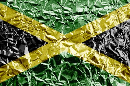 Jamaica flag depicted in paint colors on shiny crumpled aluminium foil close up. Textured banner on rough backgroundの写真素材