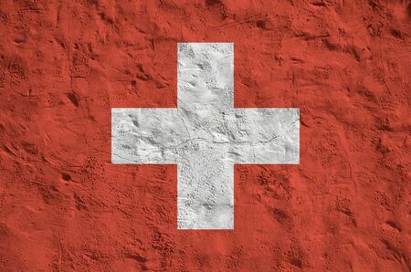 Switzerland flag depicted in bright paint colors on old relief plastering wall close up. Textured banner on rough backgroundの写真素材