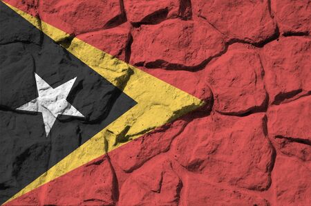Timor Leste flag depicted in paint colors on old stone wall close up. Textured banner on rock wall backgroundの写真素材
