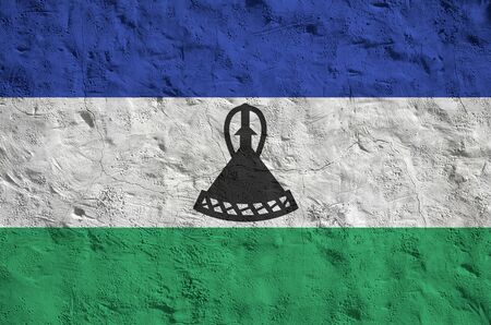 Lesotho flag depicted in bright paint colors on old relief plastering wall close up. Textured banner on rough backgroundの写真素材