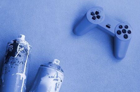 Teenagers and youth lifestyle concept. Joystick and two spray cans lies on the blanket of furry pink...