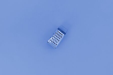 Stainless steel grater lies on a phantom classic blue paper. Kitchen accessories. Tools for cooking. Flat lay top view.の写真素材