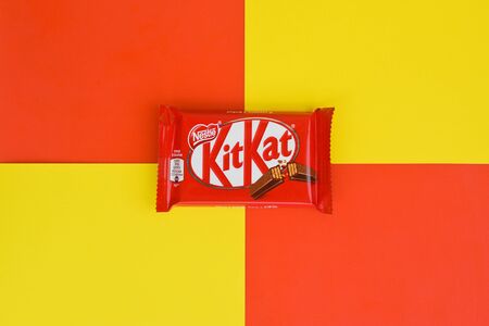 NY, USA - DECEMBER 4, 2019: Kit Kat chocolate bars in red wrapping lies on yellow and red background. Kit kat created by Rowntree's of York in United Kingdom and is now produced globally by Nestleのeditorial素材