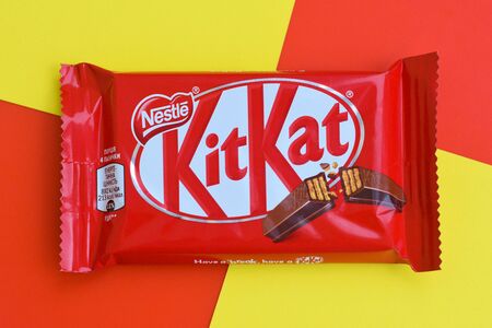 NY, USA - DECEMBER 4, 2019: Kit Kat chocolate bars in red wrapping lies on yellow and red background. Kit kat created by Rowntree's of York in United Kingdom and is now produced globally by Nestleのeditorial素材