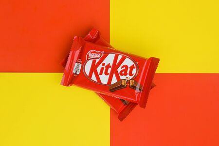 NY, USA - DECEMBER 4, 2019: Kit Kat chocolate bars in red wrapping lies on yellow and red background. Kit kat created by Rowntree's of York in United Kingdom and is now produced globally by Nestleのeditorial素材