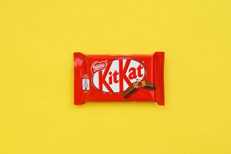 NY, USA - DECEMBER 4, 2019: Kit Kat chocolate bar in red wrapping lies on yellow background. Kit kat...