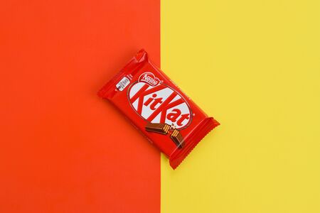 NY, USA - DECEMBER 4, 2019: Kit Kat chocolate bars in red wrapping lies on yellow and red background. Kit kat created by Rowntree's of York in United Kingdom and is now produced globally by Nestleのeditorial素材