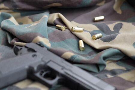 9mm bullets and pistol lie on folded camouflage green fabric. A set shooting range items or a self-defense kit. Golden shells near handgunの写真素材