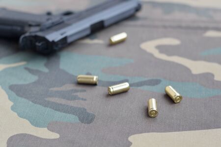 9mm bullets and pistol lie on camouflage green fabric. A set shooting range items or a self-defense kit. Golden shells near handgunの写真素材