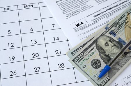 Form W-4 Employee's withholding allowance certificate and blue pen with dollar bills lies on office...