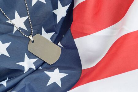 Silvery military beads with dog tag on United States fabric flag. Army token on USA banner close up....