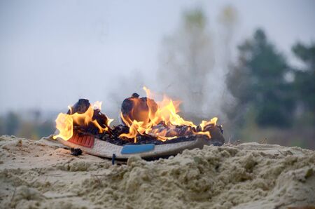 Burning sports sneakers or gym shoes on fire stand on sandy beach coast close up. Athlete burned out. Physical exertion during training conceptの写真素材
