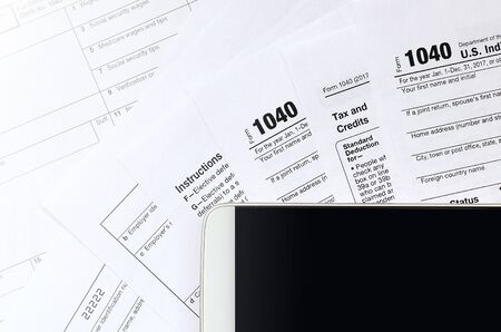 The smartphone lies on the tax form 1040 and W-2. Clean black screen smartphone for text placement