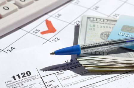 1120 Corporation Income Tax Return blank with credit card on dollar bills, calculator and pen on...