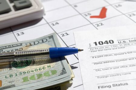 1040 Individual Income Tax Return blank with dollar bills, calculator and pen on calendar page with marked 15th April. Tax period concept. IRS Internal Revenue Serviceの写真素材