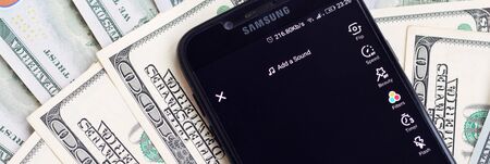 KHARKOV, UKRAINE - FEBRUARY 16, 2020: Smartphone screen with Tiktok app and lot of hundred dollar...