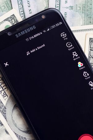 KHARKOV, UKRAINE - FEBRUARY 16, 2020: Smartphone screen with Tiktok app and lot of hundred dollar bills. Business and social networking conceptのeditorial素材