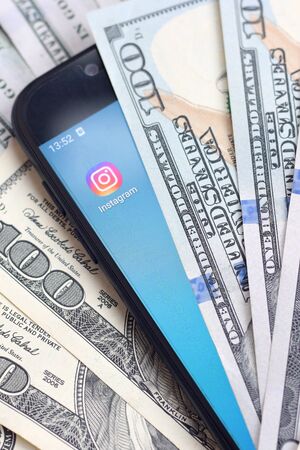 KHARKOV, UKRAINE - FEBRUARY 6, 2020: Smartphone screen with Instagram app and lot of hundred dollar bills. Business and social networking conceptのeditorial素材