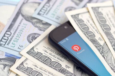 KHARKOV, UKRAINE - FEBRUARY 6, 2020: Smartphone screen with Pinterest app and lot of hundred dollar bills. Business and social networking conceptのeditorial素材