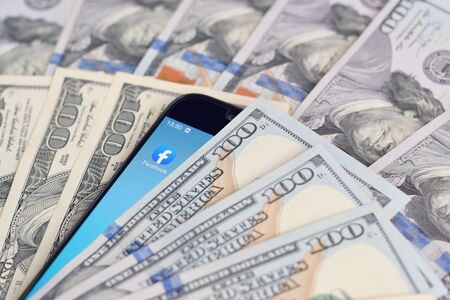 KHARKOV, UKRAINE - FEBRUARY 6, 2020: Smartphone screen with Facebook app and lot of hundred dollar bills. Business and social networking conceptのeditorial素材