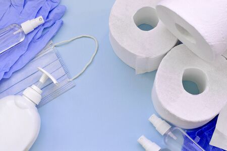 Set of important items for Covid-19 quarantine times. Toilet paper, rubber disposable gloves with surgical face mask and hand sanitizer with liquid soap bottle on blue backgroundの写真素材