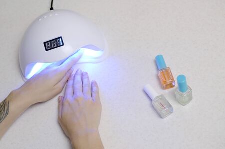 Hands of young woman at manicure procedure close up on white background. Woman Nail Polish process. Female using shellac uv led lamp for quick dryingの写真素材