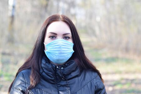Portrait of young brunette woman in blue protective mask outdoors in spring wood. Concept of protective goods usage during quarantineの写真素材