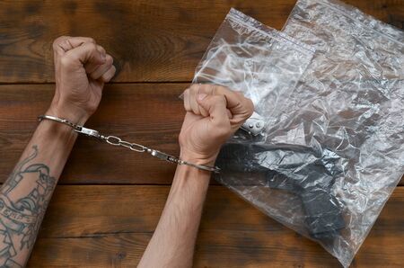Handcuffed hands of criminal suspect on wooden table and crime scene evidence in transparent plastic...