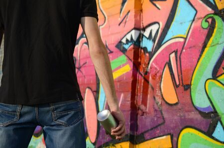 Young graffiti artist with backpack and gas mask on his neck paints colorful graffiti in pink tones on brick wall. Street art and contemporary painting process. Entertainment in youth subcultureの写真素材